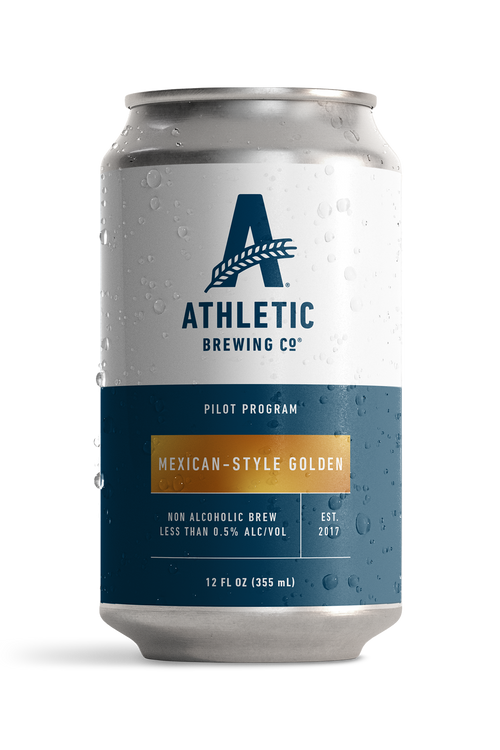 12 fl oz can of Athletic Brewing Pilot Program Mexican-Style Golden non-alcoholic brew with a clean white and navy label accented by a gold nameplate. The can is covered in condensation droplets and features the Athletic Brewing logo, “Pilot Program” branding, and product details including “Less Than 0.5% Alc/Vol.” The can is photographed against a black background, highlighting the limited-release beer packaging.