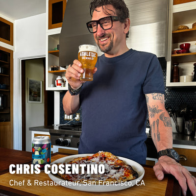 Chris Cosentino smiling, holding a glass of Aftershif non-alcoholic brew standing over pizza