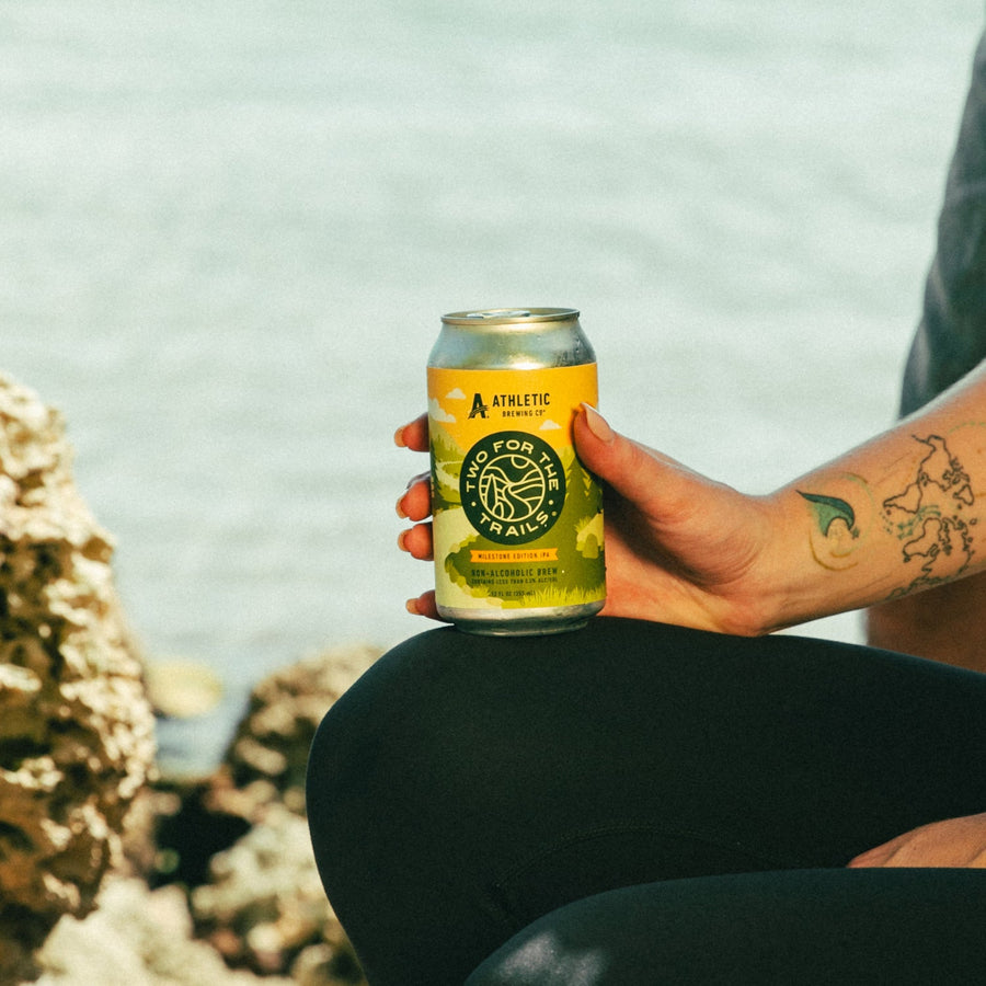 A close-up of a hand holding a condensation-covered can of Two for The Trails Milestone Edition IPA during a hike.