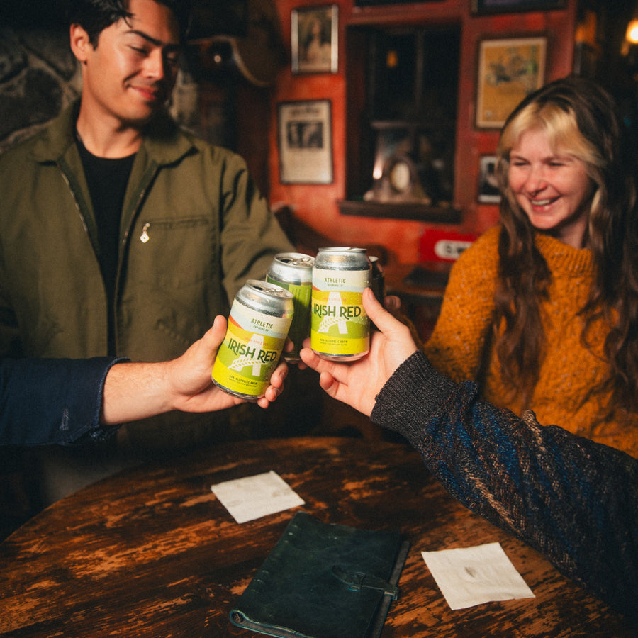Friends toasting with cans of Irish Red in a pub.